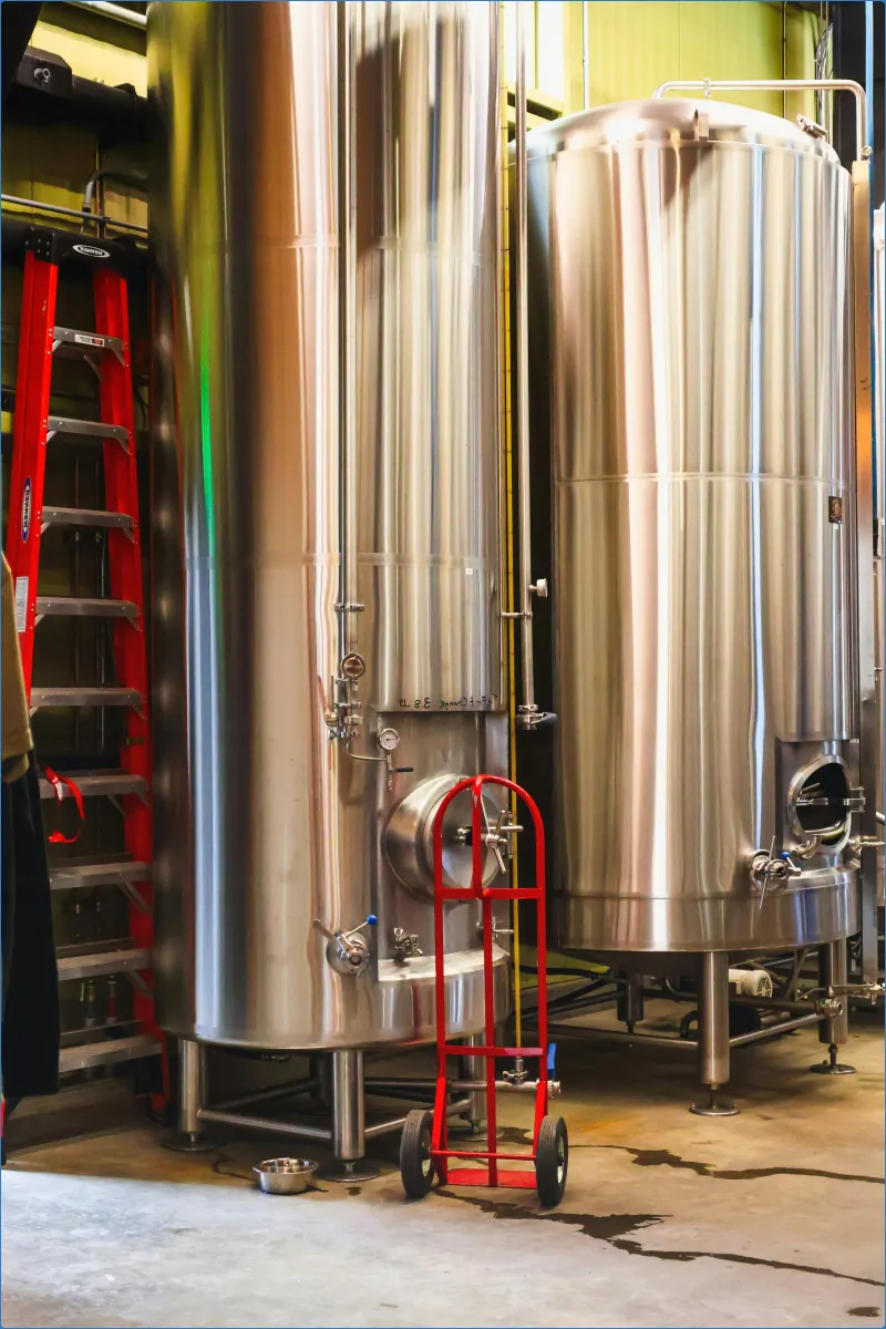 Stainless steel tanks in a brewery with a red hand truck.