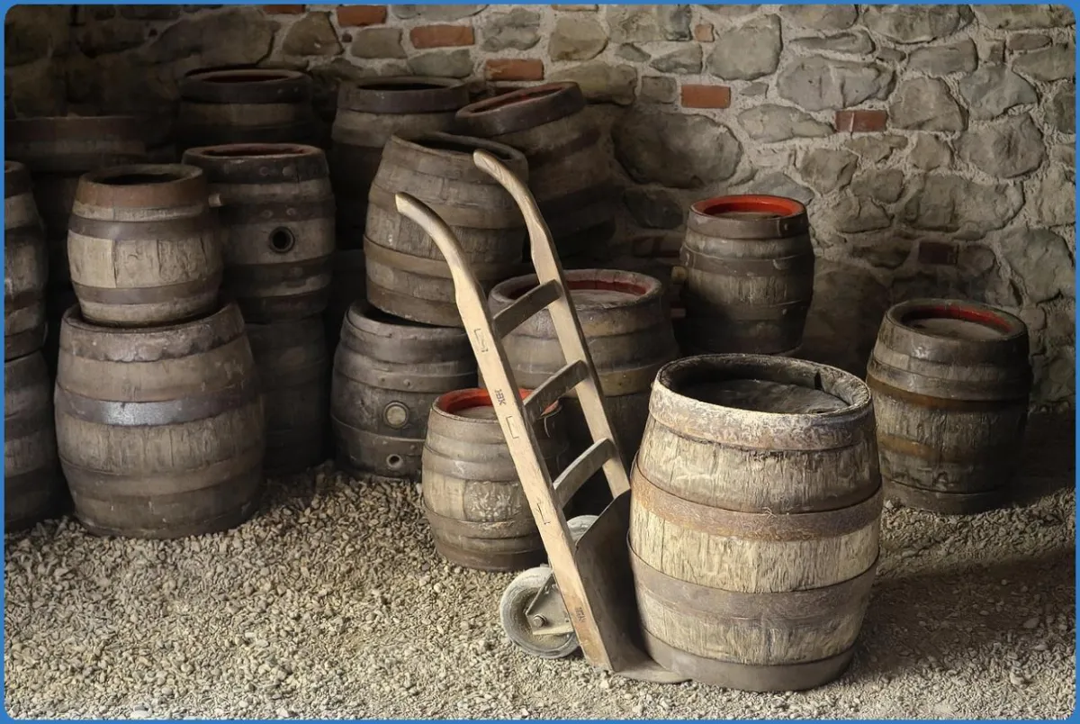 Wooden barrels with a hand truck in a stone cellar.