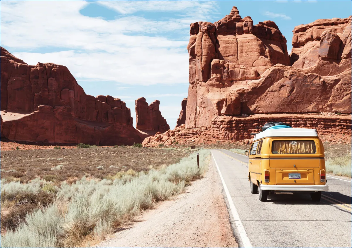 Yellow van driving through desert canyon landscape.
