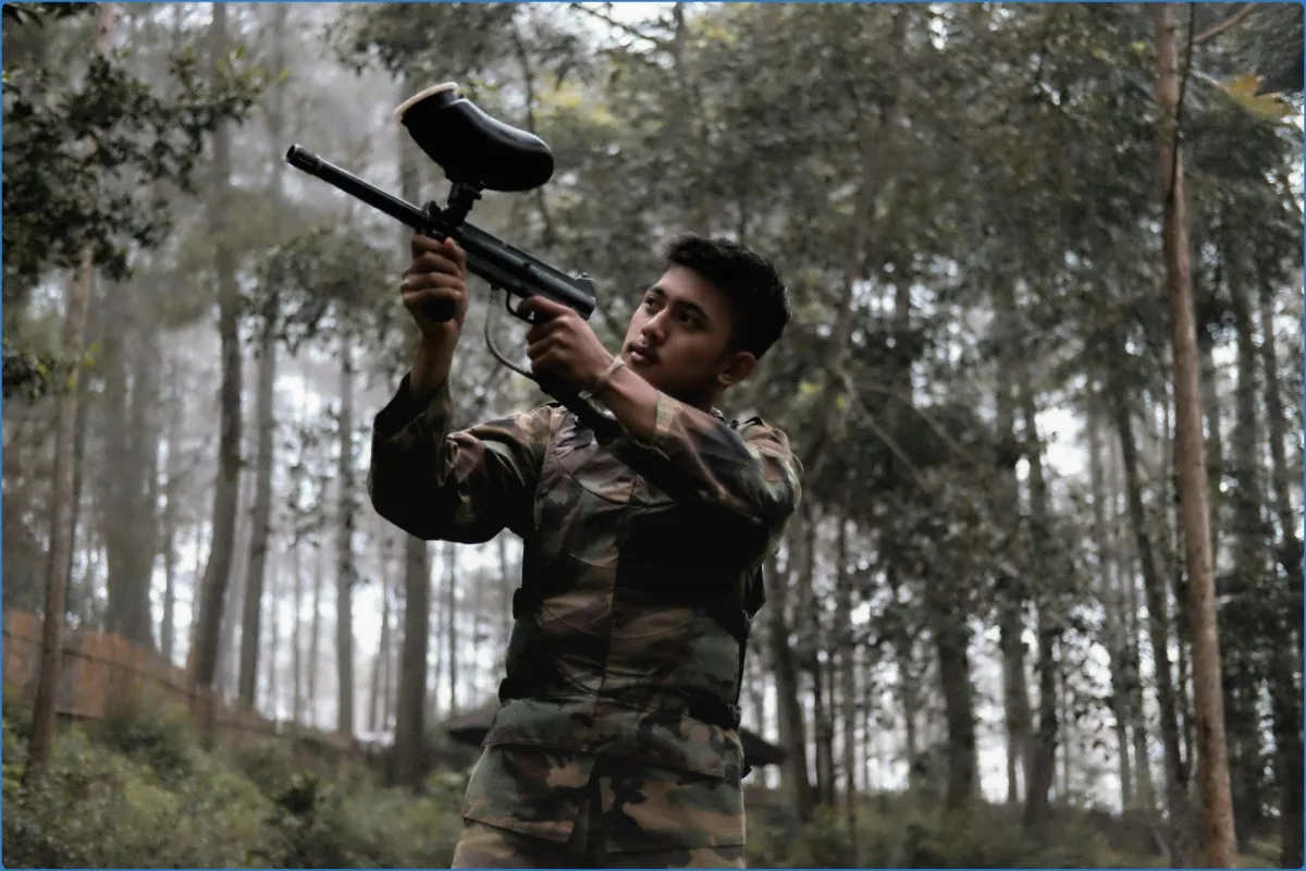 Person in camouflage holding a paintball gun in a forest