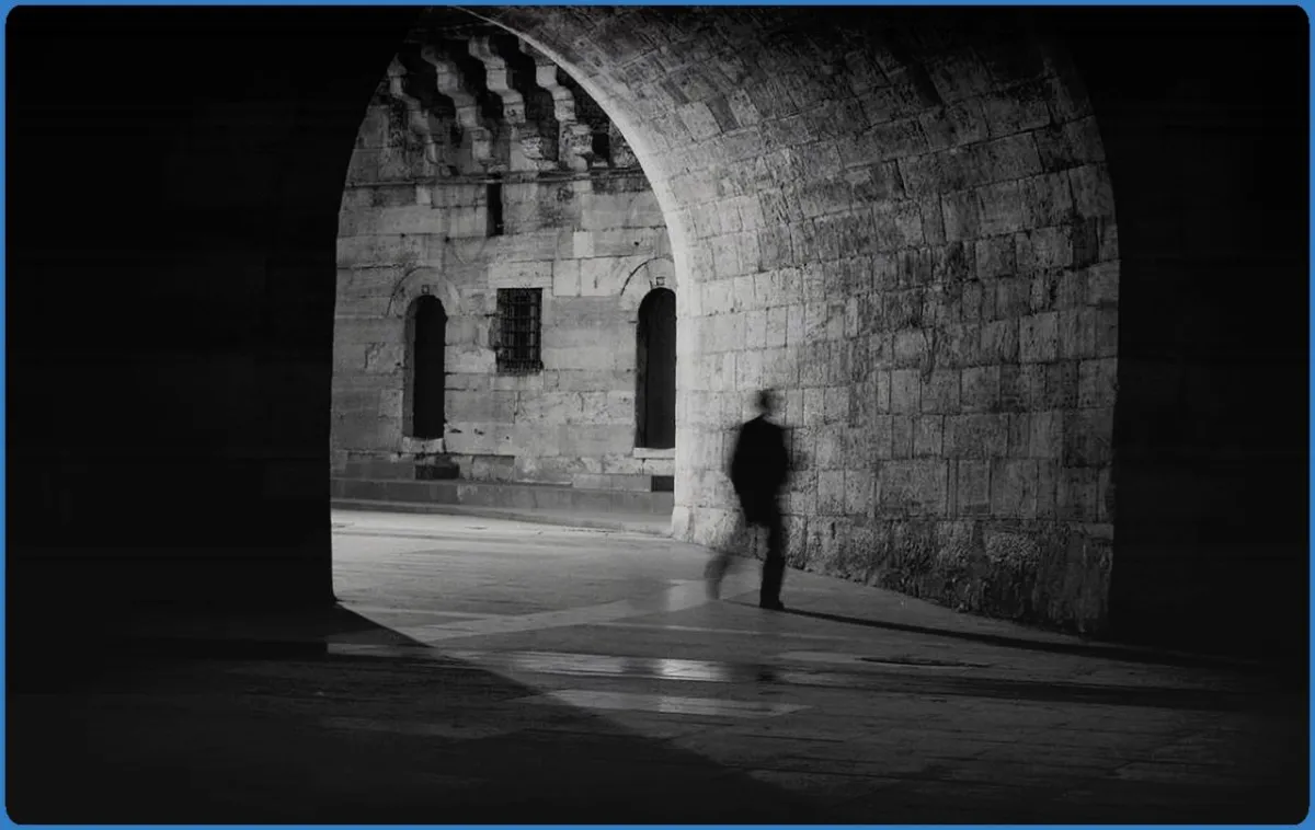 Silhouette of a person walking in a stone archway.