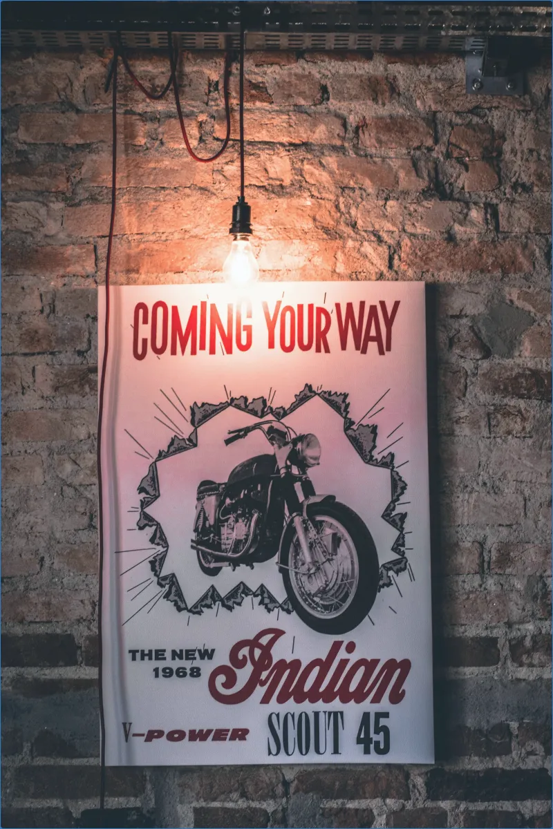 Vintage motorcycle poster on brick wall under light bulb.