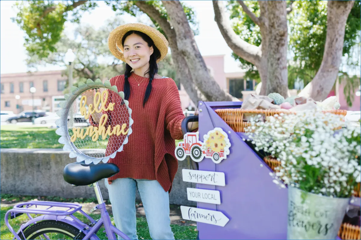 Smiling woman with a bicycle and flowers in a park.