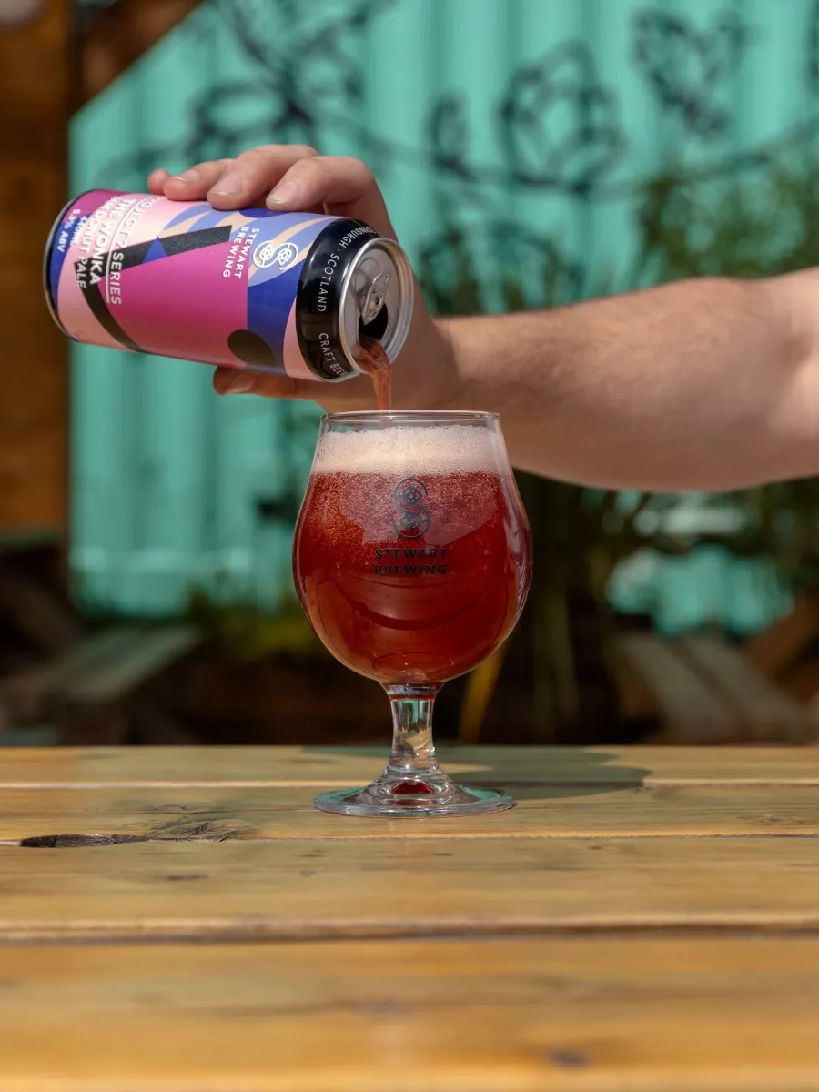 Pouring beer from can into a glass on a table.