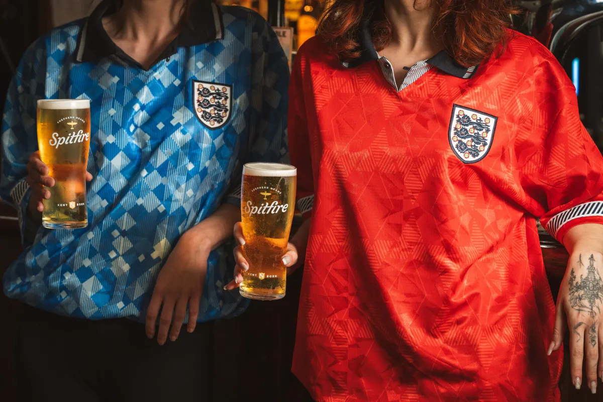 Two people in football jerseys holding pints of beer.