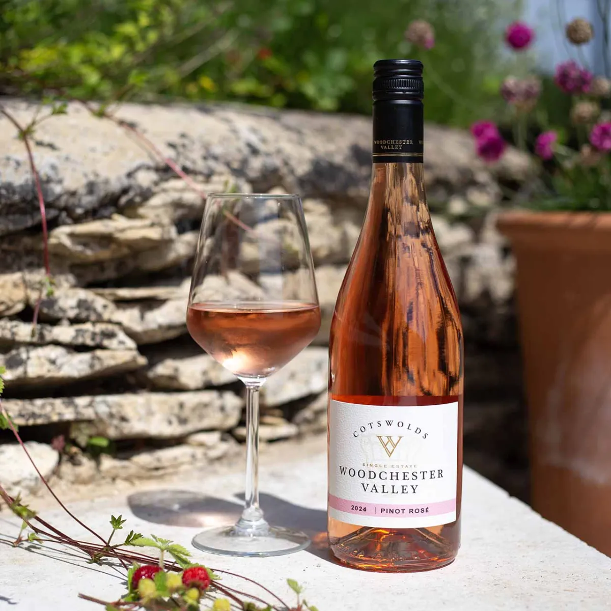 Bottle and glass of rosé wine on a stone surface.